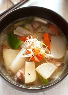 a bowl filled with meat and vegetables on top of a white wooden table next to chopsticks