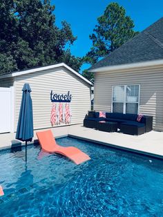 an empty pool with lounge chairs and umbrellas in front of a small white house