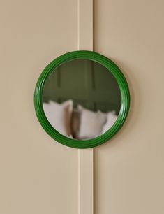 a green circular mirror hanging on the side of a wall next to a white bed