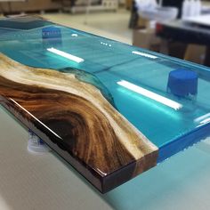 a glass table with wood and blue water in the center, on top of a white surface