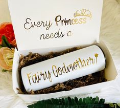 a white box with gold lettering on it next to flowers and a sign that says, every princess needs a fairy godmoten