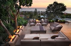 an outdoor living area with couches and fire pit in the middle, overlooking the ocean