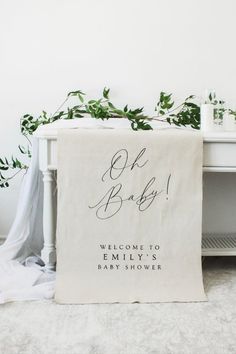 a welcome baby banner on the floor next to a white dresser with greenery in it