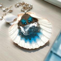 a sea shell with two blue butterflies on it next to some pearls and other jewelry