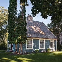 a small blue house with white windows and shingles on the roof is surrounded by trees