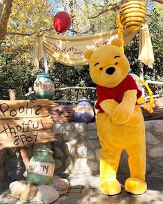 a large winnie the pooh mascot standing in front of a stone wall and sign