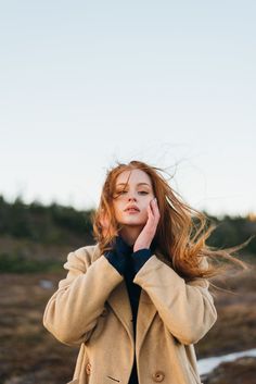 a woman with long red hair is talking on her cell phone while standing in the grass