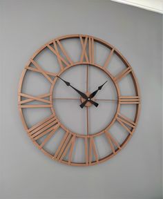 a large wooden clock with roman numerals is on the wall in an empty room