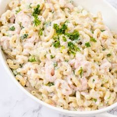 macaroni salad with chicken and parsley in a white bowl on a marble surface