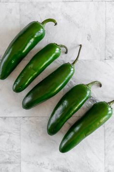 three green peppers sitting on top of a marble counter