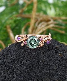 a ring with an aqua and purple stone in the center on top of a pile of dirt