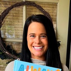 a woman holding up a book in front of a wreath with the word always written on it