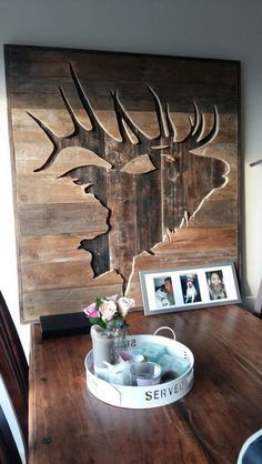 a wooden table topped with a vase filled with flowers next to a framed deer head