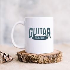 a white coffee mug sitting on top of a piece of wood next to a pine cone