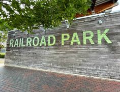 a sign that reads railroad park painted on the side of a wooden wall next to a tree