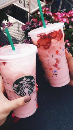 two people holding up pink drinks with green straws