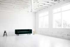 an empty white room with a green couch in the middle and two stools next to it