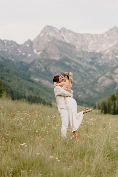 a man and woman hug in a field with mountains in the background