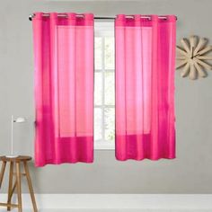 a window with pink sheer curtains in front of a white wall and wooden stools