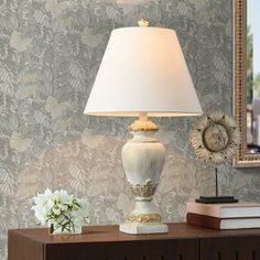 a white lamp sitting on top of a wooden table next to a mirror and flowers