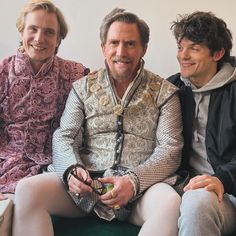 two men and a woman sitting on a couch smiling at the camera while one man holds a small object in his hand