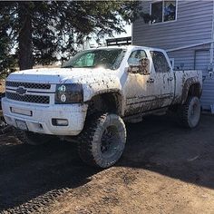 a white truck with mud all over it's tires parked in front of a house