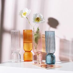 three different colored vases with flowers in them on a white countertop next to a window