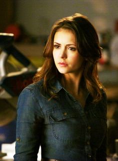 a woman with long dark hair wearing a jean jacket and looking off into the distance