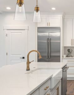 a kitchen with white counter tops and gold accents on the lights over the sink is surrounded by stainless steel appliances