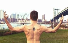 a shirtless man standing in front of a bridge with his hands up and fingers raised