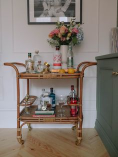 a wicker bar cart with drinks and liquor on it in front of a painting