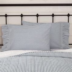 a bed with blue and white striped sheets on top of it next to a black metal headboard