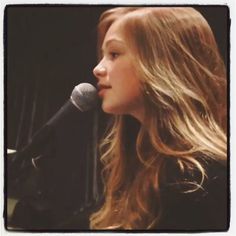 a woman with long hair holding a microphone in front of her face and looking off to the side