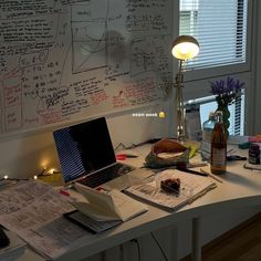 a laptop computer sitting on top of a desk covered in notes and writing paper next to a lamp