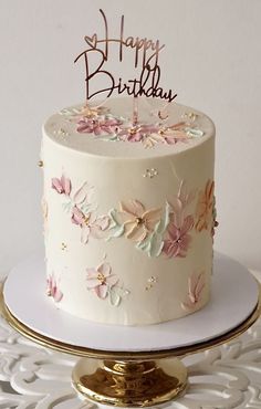 a white birthday cake with pink flowers and the words happy birthday on top is sitting on a gold platter