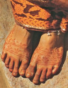 the feet and ankles of a person with hendi tattoos on their legs, in front of a stone floor