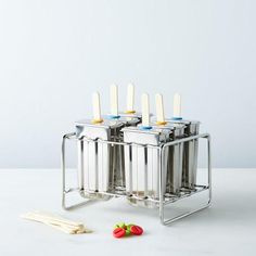 four stainless steel containers with spoons and toothbrushes in them on a white surface