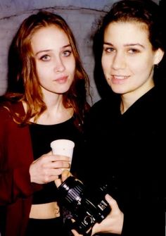 two young women standing next to each other holding coffee cups and looking at the camera