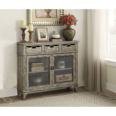 an old gray cabinet with glass doors and drawers in front of a painting on the wall