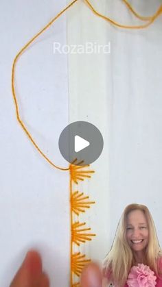 a woman holding a pink flower in front of a white wall with an orange measuring tape