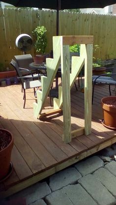 a wooden deck with chairs and an umbrella in the middle of it next to potted plants