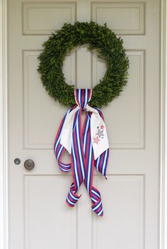 a wreath is hanging on the front door with ribbon around it and an american flag bow