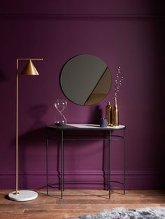 a table with a mirror and two wine glasses on it in front of a purple wall