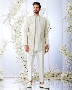 a man in a white outfit standing next to a floral wall with flowers on it