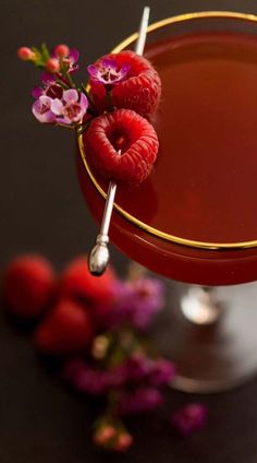 a close up of a drink in a glass with raspberries on the rim