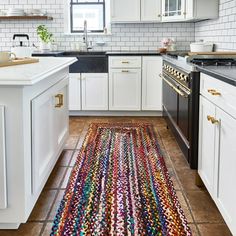 a kitchen with white cabinets, black counters and a multicolored rug on the floor