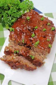 meatloaf with sauce and parsley on a white plate next to green vegetables