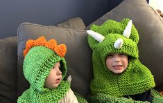 two children wearing green knitted hats and scarves sitting on a couch with pillows