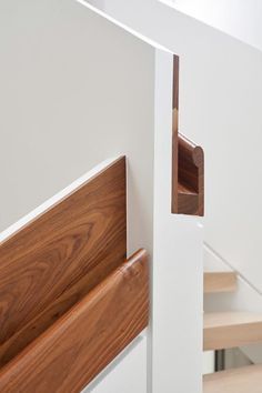 a wooden handrail on the side of a white wall next to some stairs and railings