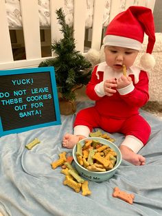 a baby in a santa hat sitting on a blanket eating crackers next to a sign that says yuck do not leave the cookies out for santa